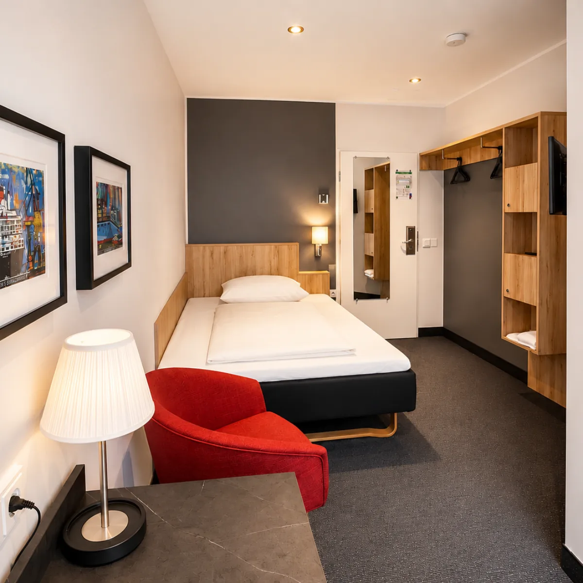 Einzelzimmer im EGON HOTEL · Bett mit Hamburg-Kunstdrucken und rotem Sessel